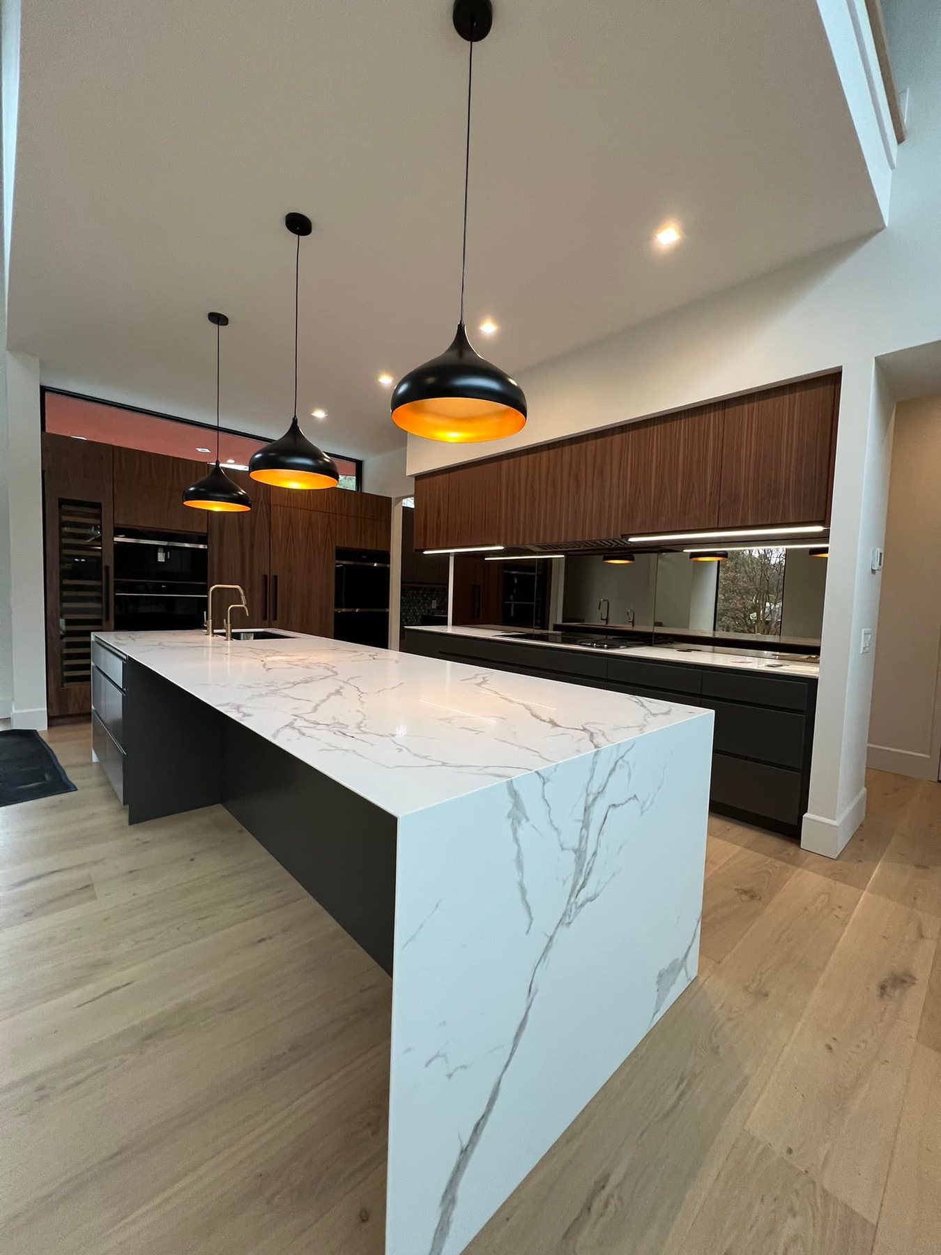 Custom kitchen with a marble waterfall island and dark flat panel cabinetry