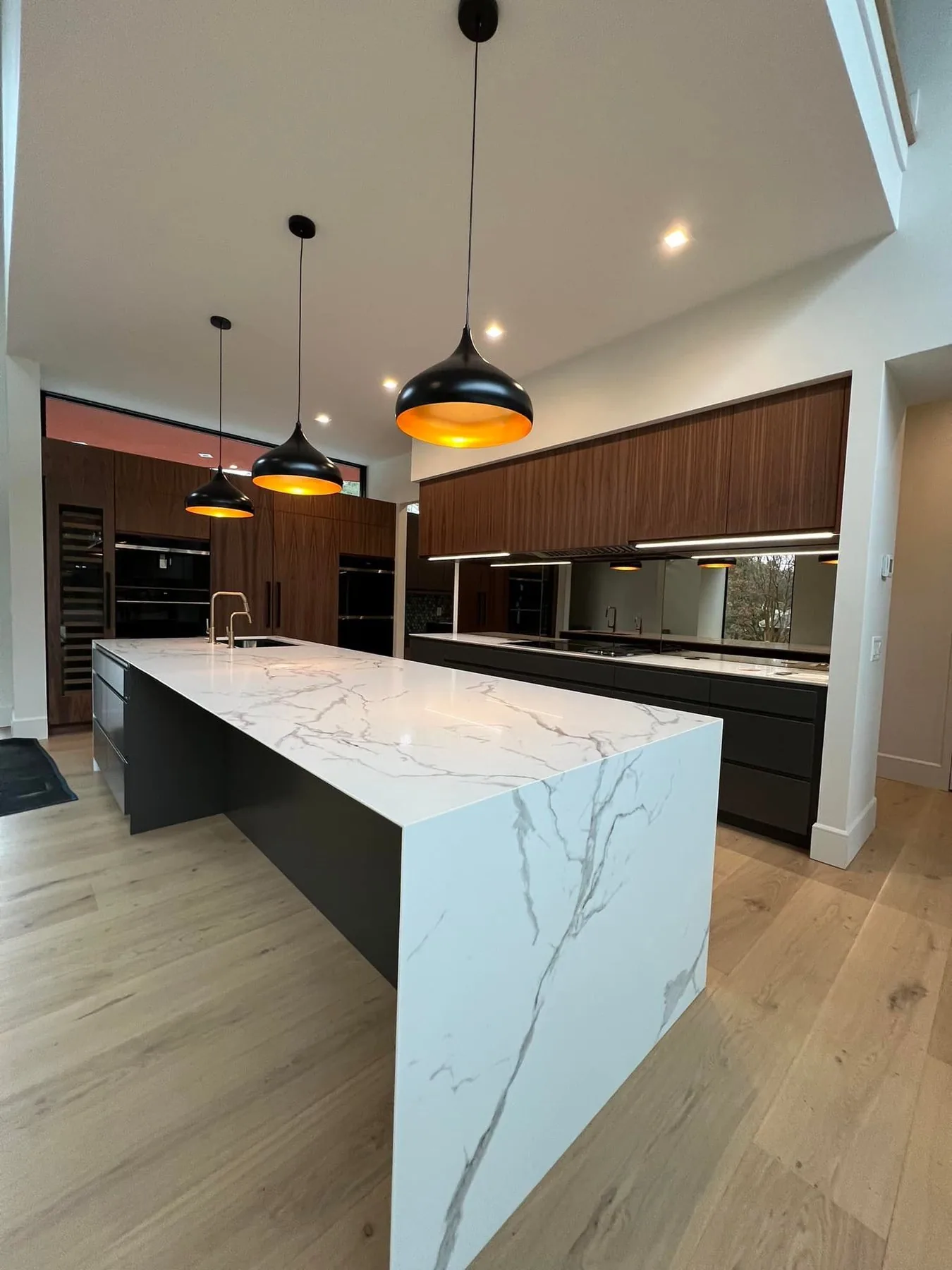 Custom kitchen with a marble waterfall island and dark flat panel cabinetry