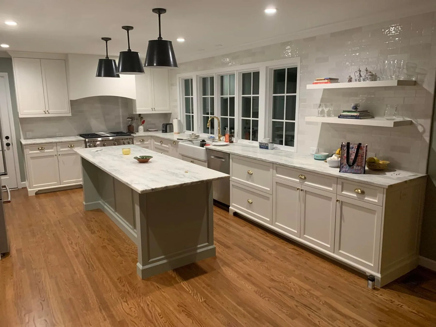 Custom white kitchen cabinetry with a painted island, open shelving and a custom range hood